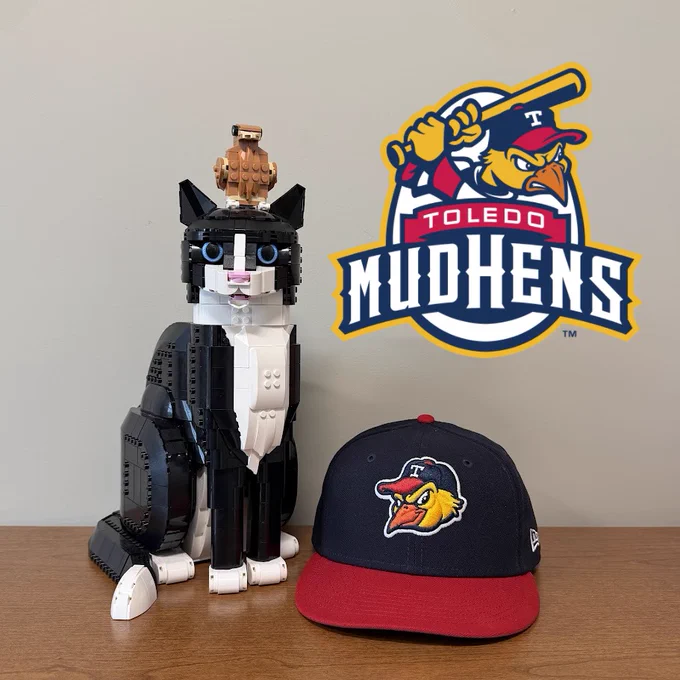 A navy blue and red Toledo Mud Hens with HATS the Lego Cat, Lil' Golden Eagle, and a Toledo Mud Hens logo.