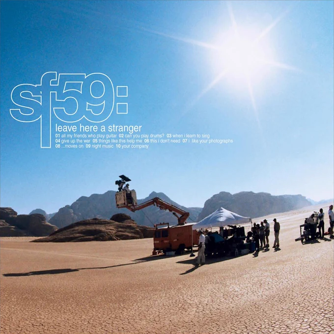 Album Art of Starflyer 59's Leave Here A Stranger album - A somewhat grainy and slightly warped wide-angle photo of some cameras and a movie crew on a desert landscape, with a camera on a large movable arm bucket and a tent with lots of people and equipment next to the base of the arm. The camera and the people are mostly looking off to the left side, but we cannot see what they are filming. The sky is blue and covers the top half of the photo, and the white, bright sun is in the middle of the top right area. Printed above the sky on the left is 'sf59:' in large white outline, with the album title in much smaller lowercase text below it, and then the track listing in even smaller text below that.