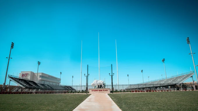 A wide view of the Citizens Bank Plaza at West Texas A&M University. The image features a clear blue sky, a central pathway leading to a buffalo statue, and surrounding stadium seating.