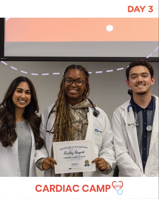 Label “Day 3” on top-right corner, shows three individuals in white coats standing together in a classroom setting. The person in the center holds a certificate of completion for “Cardiac Camp at UCLA,” while the others stand on either side wearing stethoscopes. “Cardiac Camp” text with a stylized heart icon at the bottom-center.