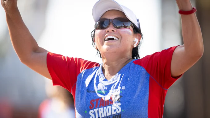 A runner holds their hands up in joy. Their shirt reads Stars and Strides.