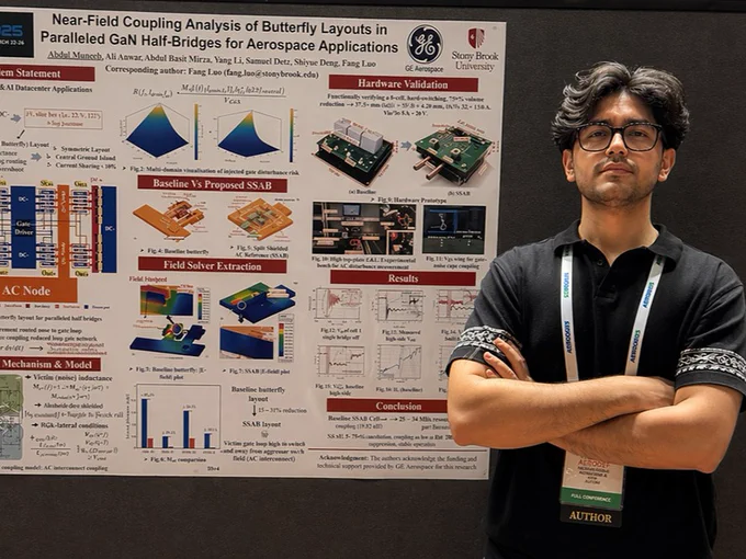 A person stands confidently in front of a scientific poster titled "Near-Field Coupling Analysis of Butterfly Layouts in Paralleled GaN Half-Bridges for Aerospace Applications." The person's arms are crossed, and a lanyard with identification is visible. The poster includes diagrams, charts, and text, featuring affiliations with Stony Brook University.
