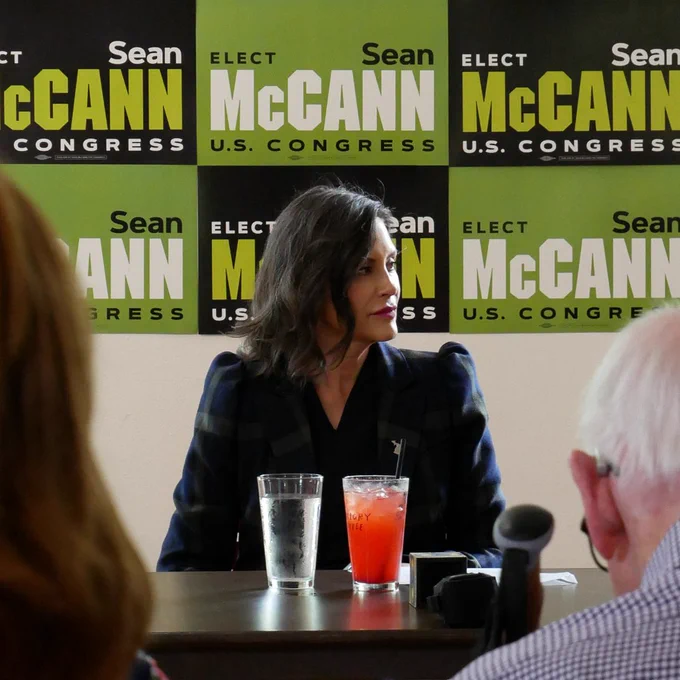 Governor Whitmer sitting in front of "Sean McCann for U.S. Congress" signs.