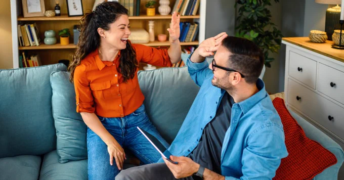 Two people high-five while sitting on their couch at home.