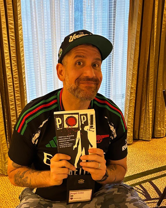 Photo of Angel Luis Colón holding a copy of his novel POP!.