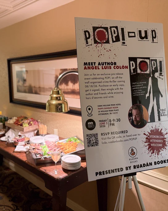 Photo of the POP!-Up Event poster on an easel in the foreground with a banquet table covered in wine and fancy snacks in the background. 