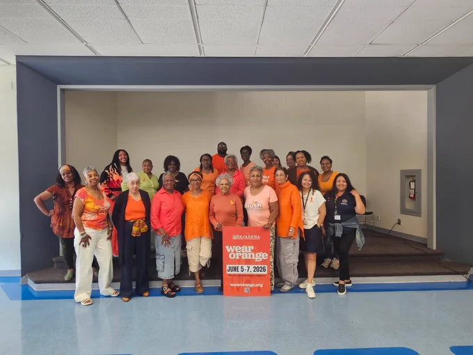 Jackie Robinson Community Center Staff stand together indoors, many wearing orange clothing. They hold a red sign that reads, "Wear Orange, June 5-7, 2023, WearOrange.org." 