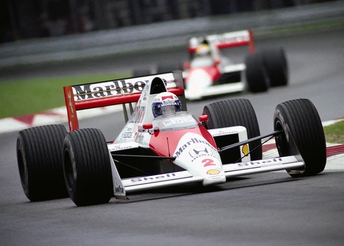 A Dutch angle shot canted slightly to the left of Alain Prost on track in the red and white, Marlboro sponsored McLaren MP4/5. It is similar to its predecessor, with an air intake visible over Prost's head. Out of focus in the background, Ayrton Senna can be seen in his MP4/5. 1989 Italian Grand Prix.
