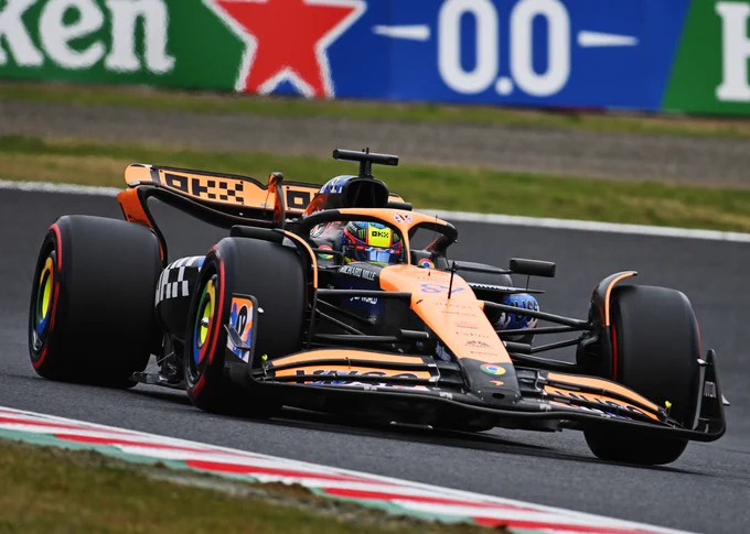 A Dutch angle shot canted slightly to the right of Oscar Piastri on track in his black and papaya McLaren MCL38. Its front and rear wings are shapely and made up of a number of pieces; it has flip-flop shaped Halo head protection, thicker suspension parts and deflectors curving over the inside of the front wheels. 2024 Japanese Grand Prix.