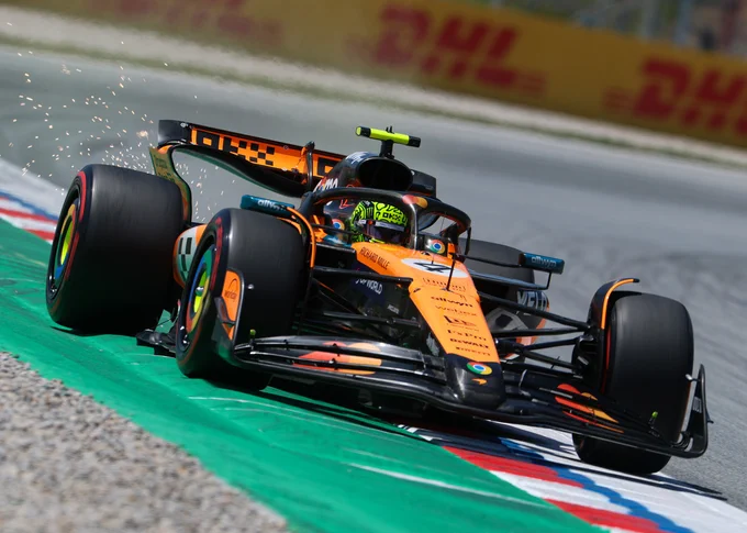 A Dutch angle shot canted slightly to the right of Lando Norris kicking up sparks over a kerb in his black and papaya McLaren MCL39. It is visually very similar to its predecessor. 2025 Spanish Grand Prix.