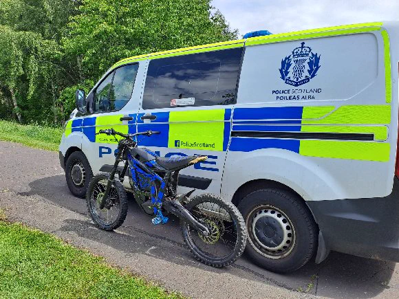 A black and blue electric dirt bike parked beside a Police Scotland van.