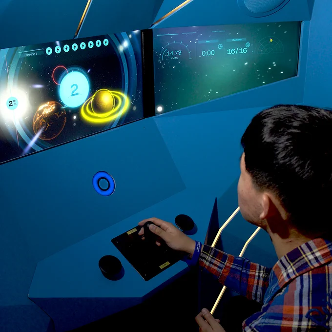 Jeune garçon assis à une console de jeu vidéo dont l’écran montre des planètes et des étoiles.