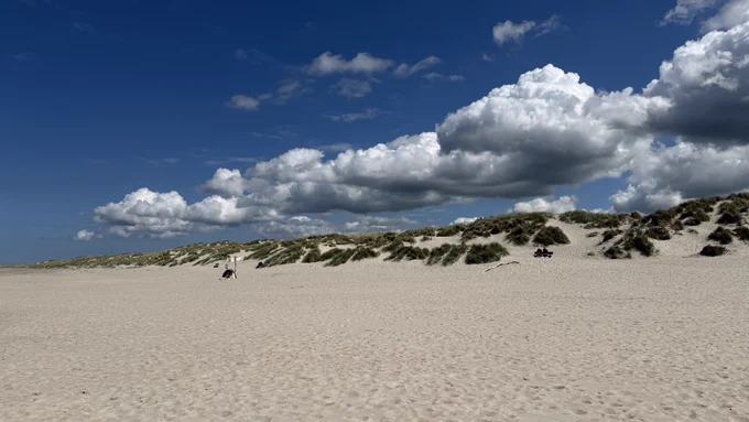 Strand mit Dünen im Hintergrund und tollen Wolken darüber mit blauem Himmel.