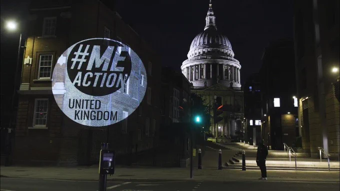 A projection of #MEAction UK's logo in white on a wall with St Paul's cathedral in the background at night.