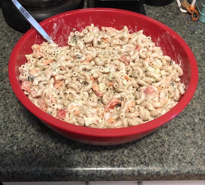 Large mixing bowl containing macaroni salad: Elbows, carrot, celery, red bell pepper, pickles, mixed with a scratch made creamy tangy dressing.