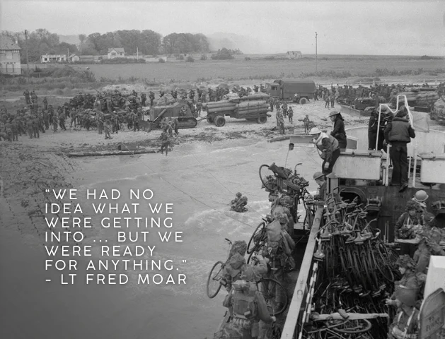 A black-and-white photo of a landing craft close to shore, heavily laden with bicycles and soldiers. A large number of soldiers are on the beach, as well as a few military vehicles. Text reads: “We had no idea what we were getting into ... But we were ready for anything.”- Lt Fred Moar