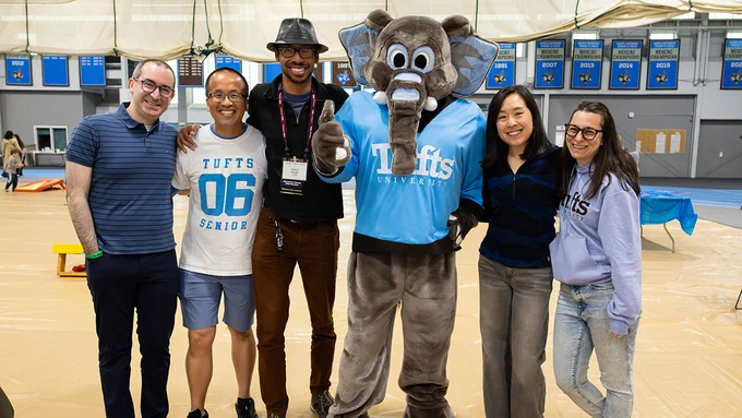 Five alumni standing with the Jumbo the elephant mascot at Ellis Oval during a Tufts Reunions event