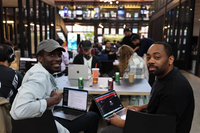 Two participants of the hackathon share their work on their laptops with the camera. They are smiling.