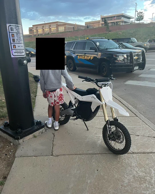Kid standing next to Emotorcycle in front of patrol car