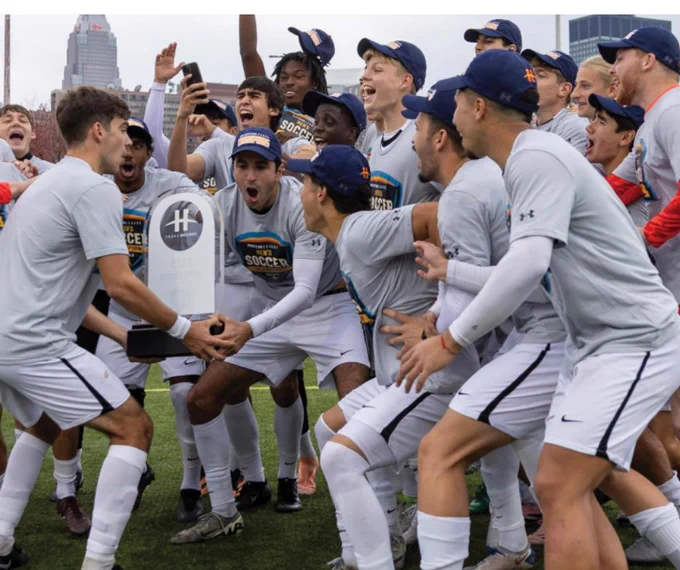 Men's soccer team cheering and lifting the Horizon League trophy. 