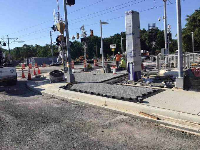 Construction workers installing tactile paving at a railway crossing under clear blue sky.