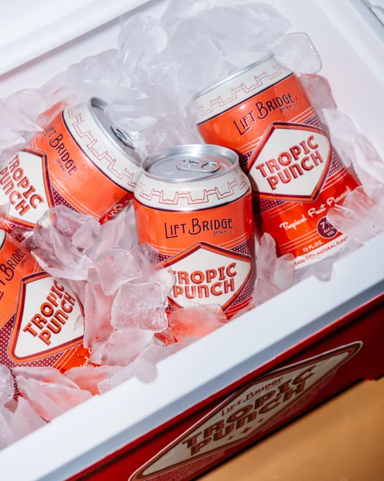Colorful Tropic Punch cans from Lift Bridge Brewing Co. are chilled in a cooler filled with ice. The vibrant red packaging adds vibrancy and signals a refreshing beverage experience.