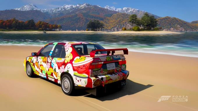 Un coche colorido con un diseño vibrante de temática de dibujos animados recorre una playa en el videojuego Forza Horizon 6. En el fondo, se aprecia una vista escénica de montañas y árboles otoñales.