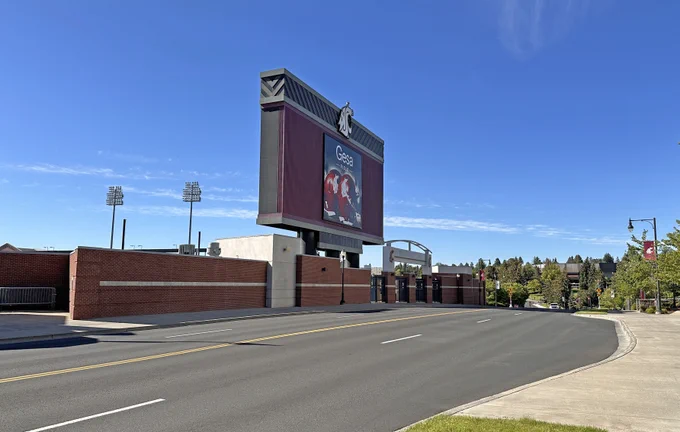 Color outdoor photo showing 4 lane Stadium Way with a large sign on the left. Blue sky and white clouds are above. 