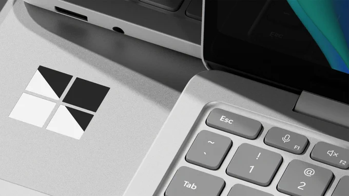Close-up view of two silver laptops on a light surface, featuring a Windows logo on one device and a detailed keyboard section on the other, including visible keys such as Esc and Tab, with soft reflections and muted lighting emphasizing the metallic finish.
