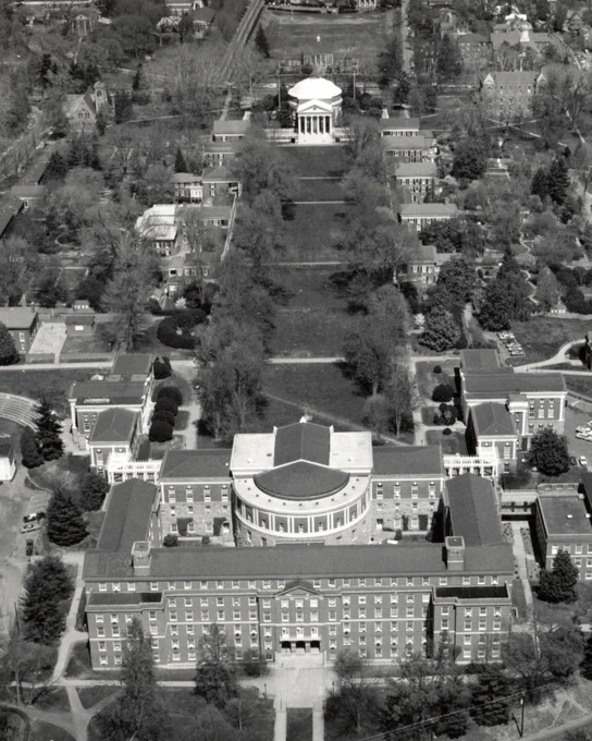 Aerial view of the University of Virginia's historic campus, featuring the Rotunda at the center, surrounded by tree-lined walkways and University buildings.