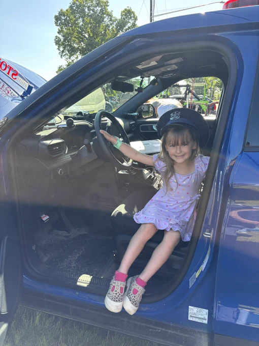 Young lady with a trooper hat on, sitting in a patrol car.