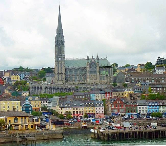 Cathedral with a tall slender spire above rows of colourfully painted  houses on the busy harbour front