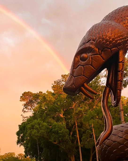 A photo of the Snake Pit statue at Innisbrook with a colorful sunset sky and rainbow in the background.
