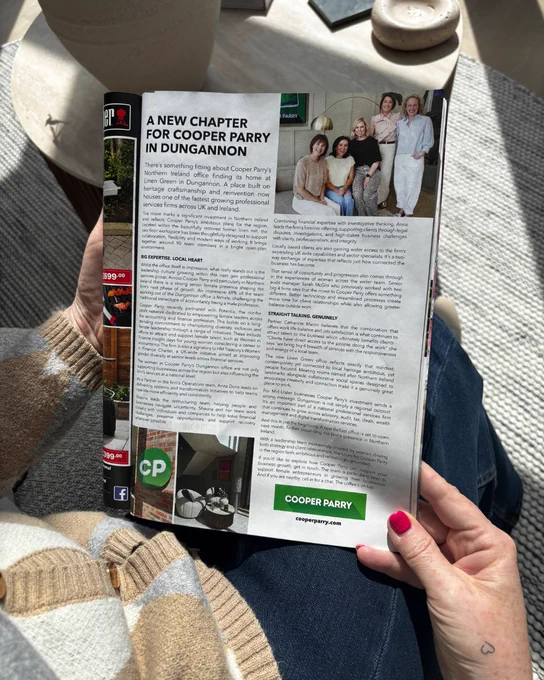 Open magazine featuring “A New Chapter for Cooper Parry in Dungannon” article, held on a sofa with soft natural light and ofice decor.