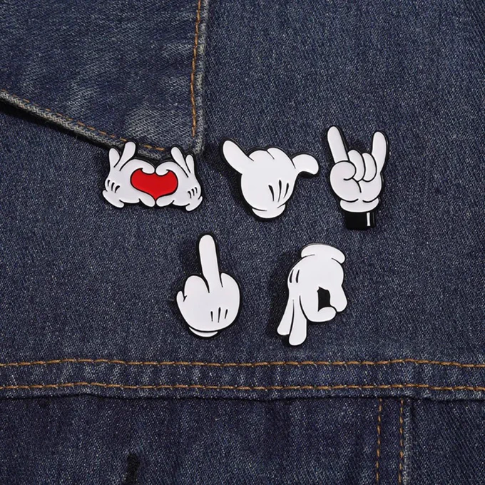 Cute cartoon finger gesture enamel pin collection displayed on a denim jacket. Fun metal lapel badges featuring love heart hands, rock sign, hand gestures, and playful cartoon designs, perfect for bags, backpacks, jackets, shirts, and casual fashion accessories. ❤️✨🖐️🎒
