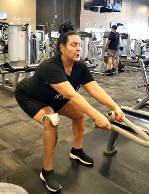 A woman in a gym doing a rope exercise, wearing a knee brace and black athletic wear.