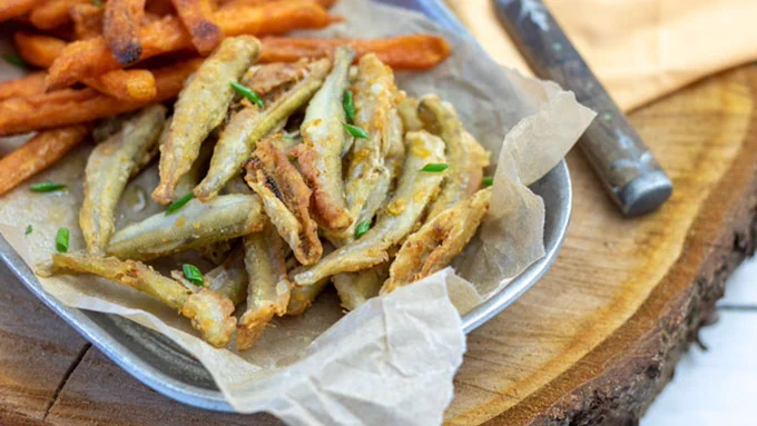 Pewter tray filled with golden fried smelt and sweet potato fries.