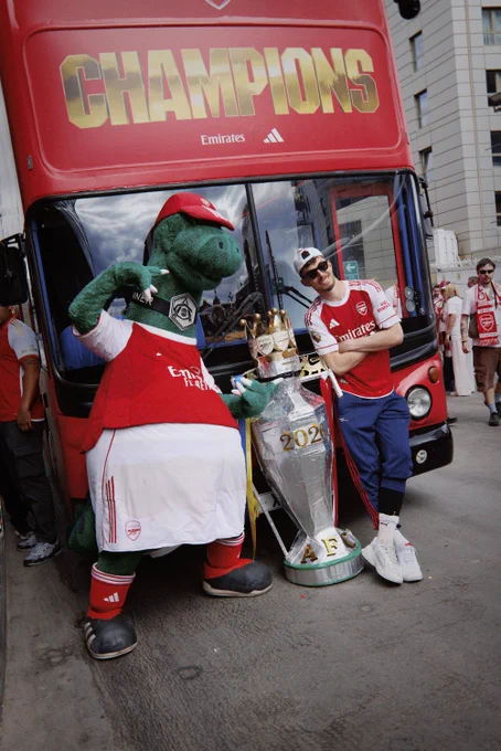 Gunnersaurus and Kai Havertz pose with a big handmade Premier League trophy outside the champions bus