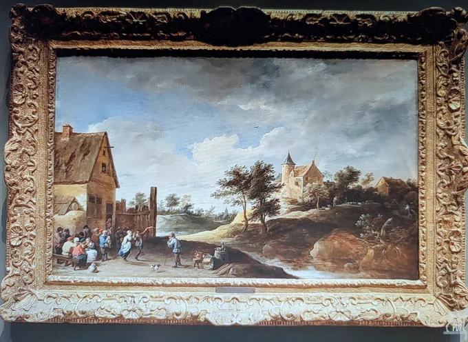 17th-century Dutch oil painting of a village with peasants dancing at left. A nearby dog standing on an embankment is looking in the other direction.