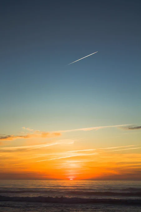 Beautiful ocean sunset just above the horizon bright orange skies and a jet plane in the distance Photography submitted to freestock by Amanda Ferreira
