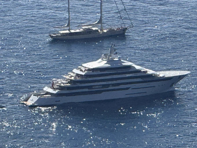 Close-up of a large white superyacht on the blue Mediterranean, with another sailboat anchored in the background.