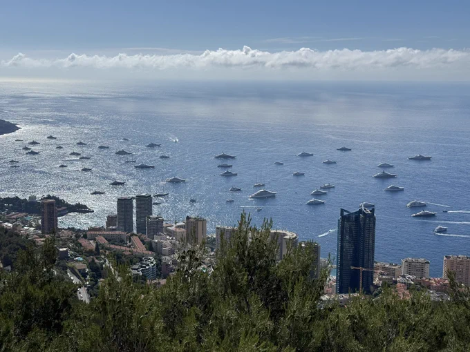 Elevated view of Monaco’s coastline and blue Mediterranean waters, with city towers below and luxury yachts spread across the bay.