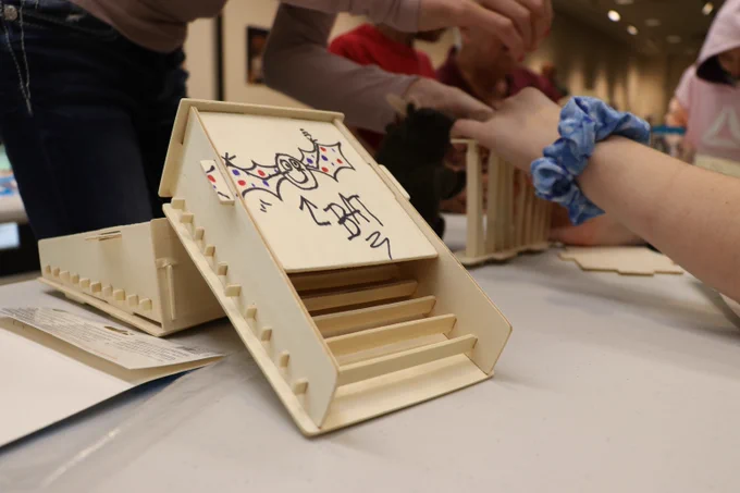 A wooden bat house is shown with others being made in the background.