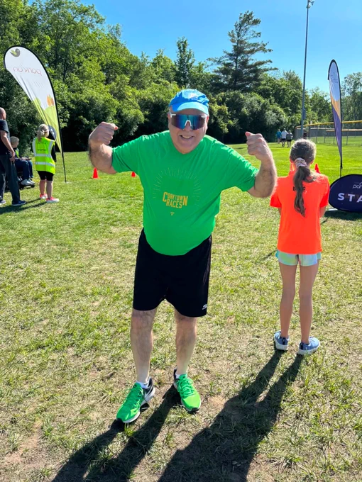 A man wearing green smiles and strikes a strong pose during outdoor exercise event.