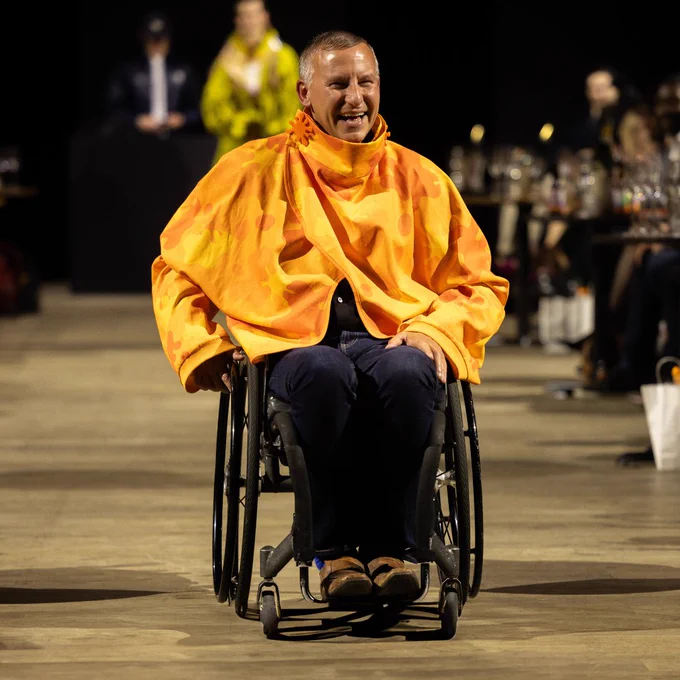 Photo of model Sean wearing an orange jacket and navy blue trousers on the Front Row runway. 