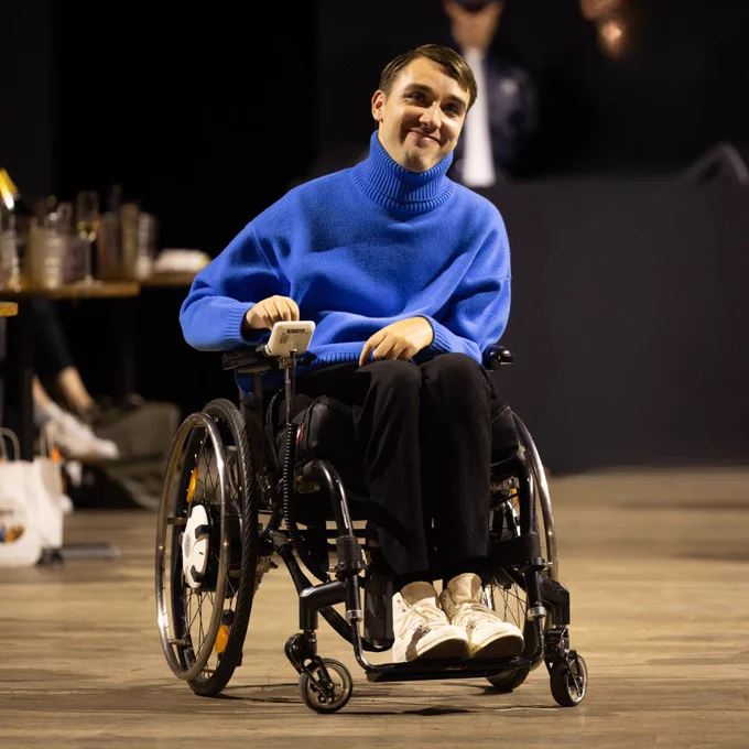 Photo of model George wearing a blue turtleneck jumper and black trousers on the Front Row runway. 