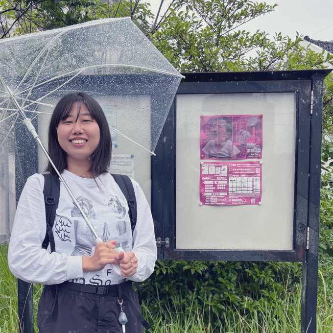 雨の中、透明なビニール傘を差して「凄ロック」のチラシが掲出された掲示板の前に立つ人物(いといけいと)