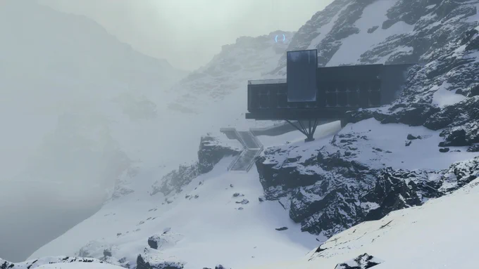 Ein markantes dunkles Gebäude an einem steilen verschneiten Berghang in Death Stranding Directors Cut. Eine lange Treppe führt ins Nichts und dicker Nebel hüllt die frostige Berglandschaft ein.