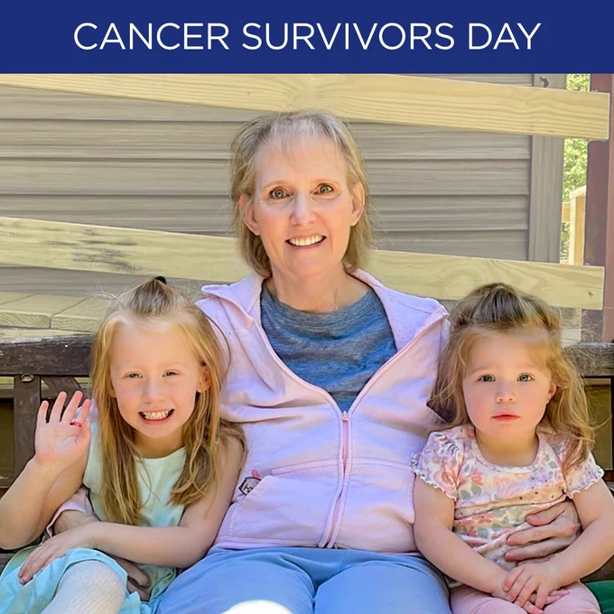 A person seated outside on a bench, smiling, with two young children on either side. One child is waving. A banner above reads "Cancer Survivors Day.