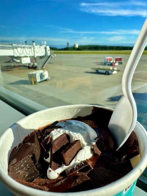 A cup of chocolate ice cream with chocolate chucks and a plastic spoon sits on a windowsill overlooking Worcester Regional Airport's airfield.